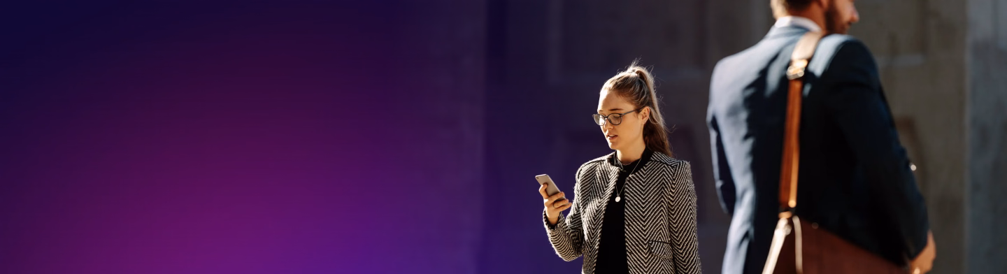 Woman looking at her phone with a man in a suit walking in the background